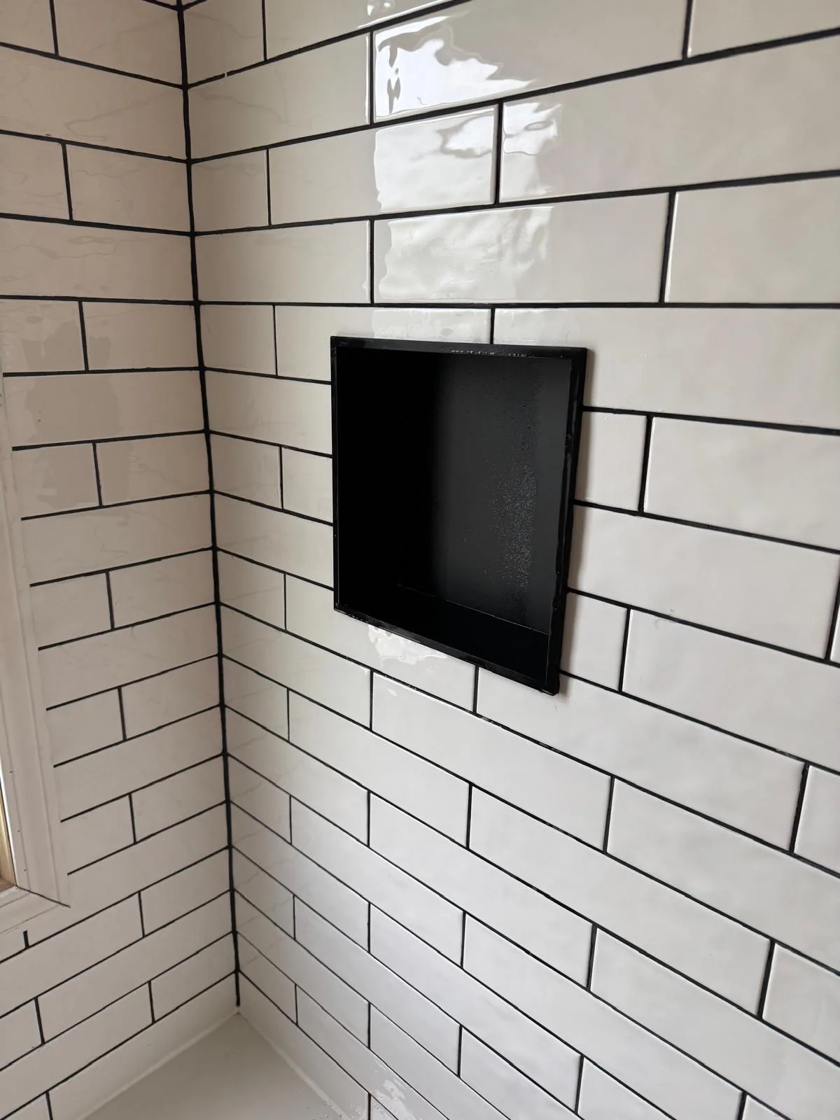 White subway tile shower with black built-in niche